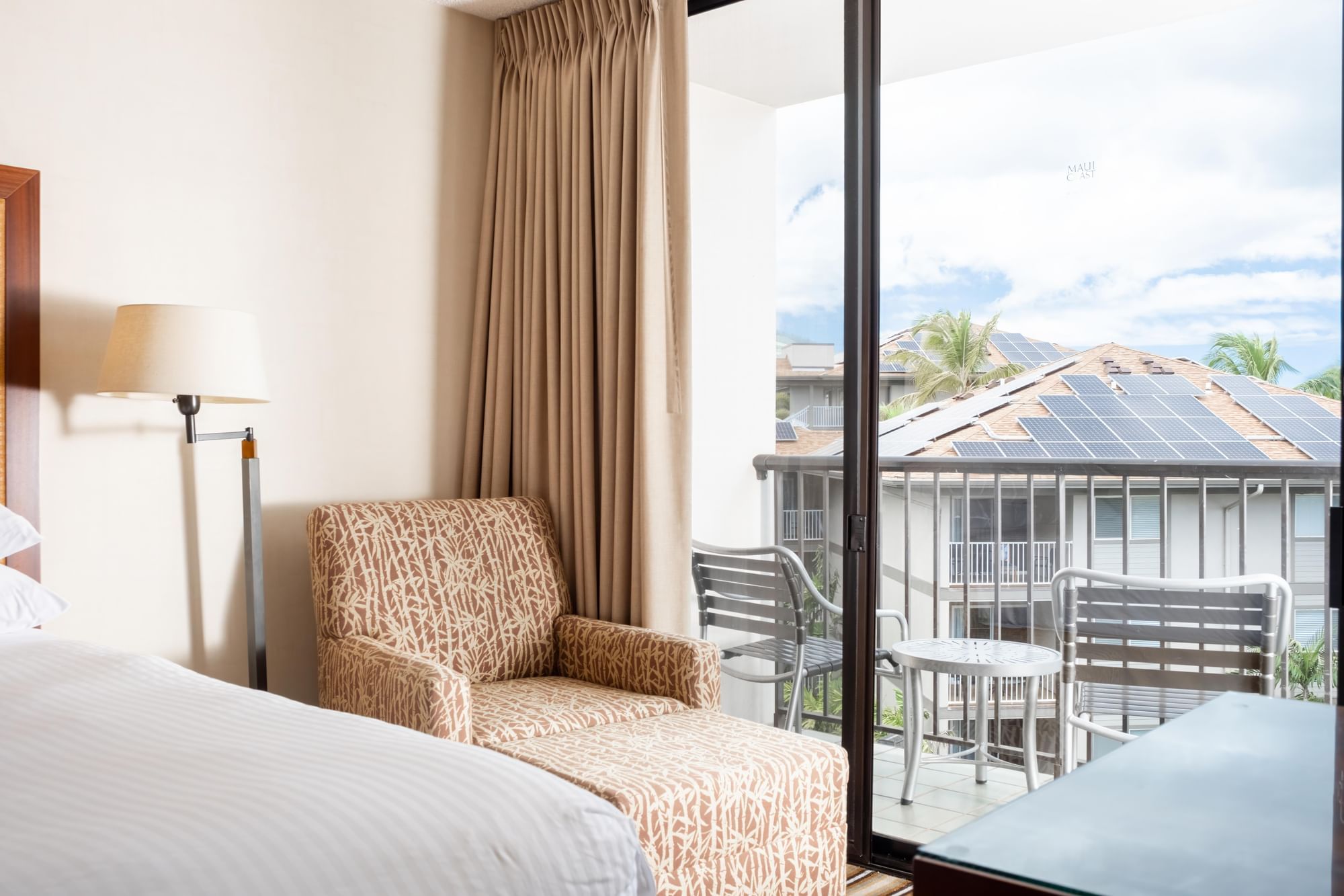 A hotel room with a bed, chair, lamp, and balcony