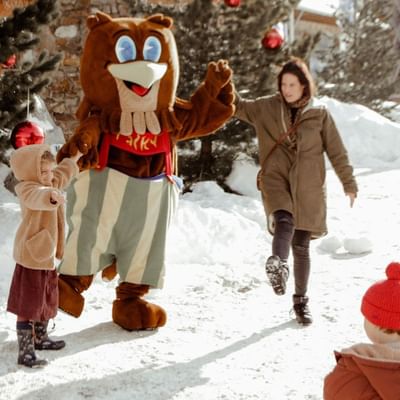 Eine Familie genießt Schneezeit mit einem Maskottchen in einem verschneiten Wald.
