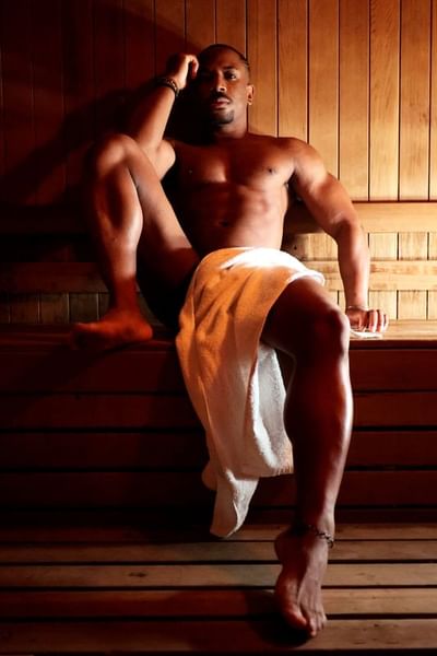 A man sits relaxed on a wooden bench in a dimly lit sauna, exuding an atmosphere of calm at The Gaythering