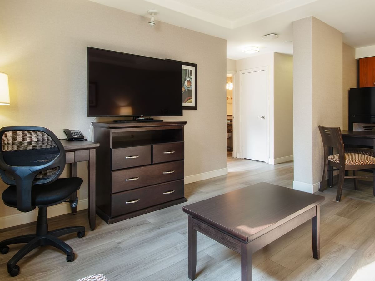 Hotel suite with TV, work desk, chair, table, and a kitchen area