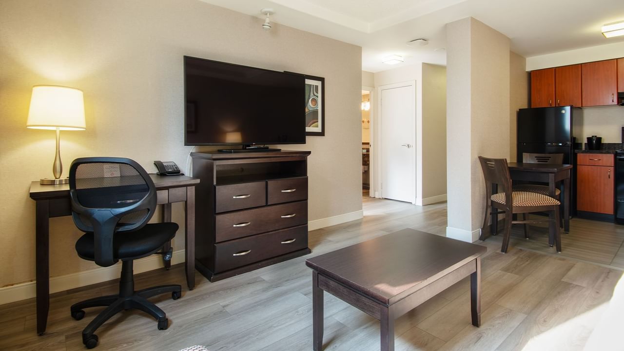 Hotel suite with TV, work desk, chair, table, and a kitchen area