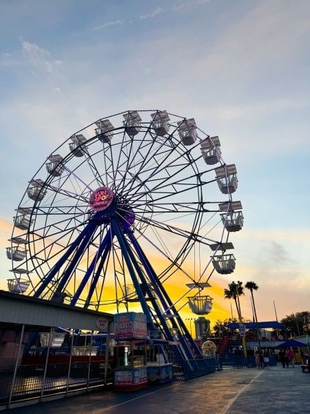 A large Ferris wheel at Fun Spot in Orlando in front of a watercolor sunset.
