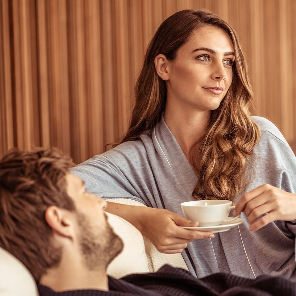 Frau hält eine Kaffeetasse neben liegendem Mann im Clubwochen Relax & Recharge Event.