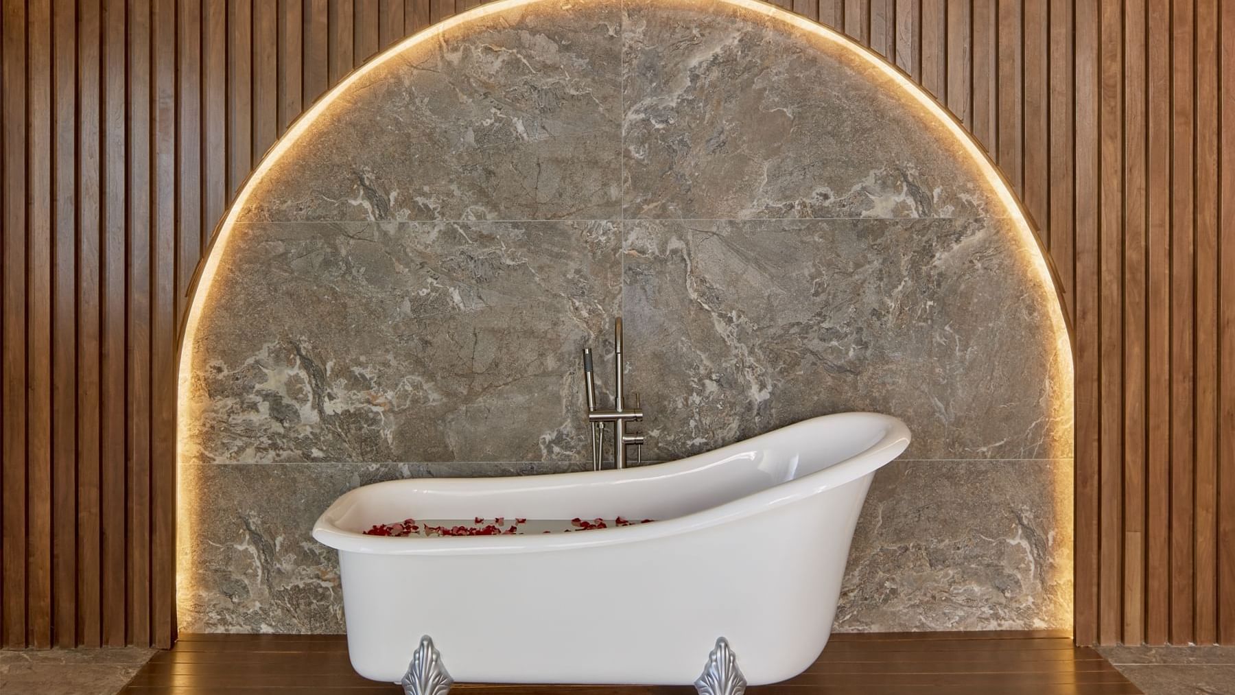 Luxurious white clawfoot bathtub with rose petals at Fiesta Americana, set against a marble and wood-paneled archway