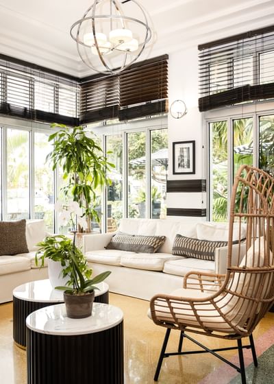 Cosy lobby sitting area at Riviera Hotel South Beach featuring a white sofa, wicker chair, and lush indoor greenery