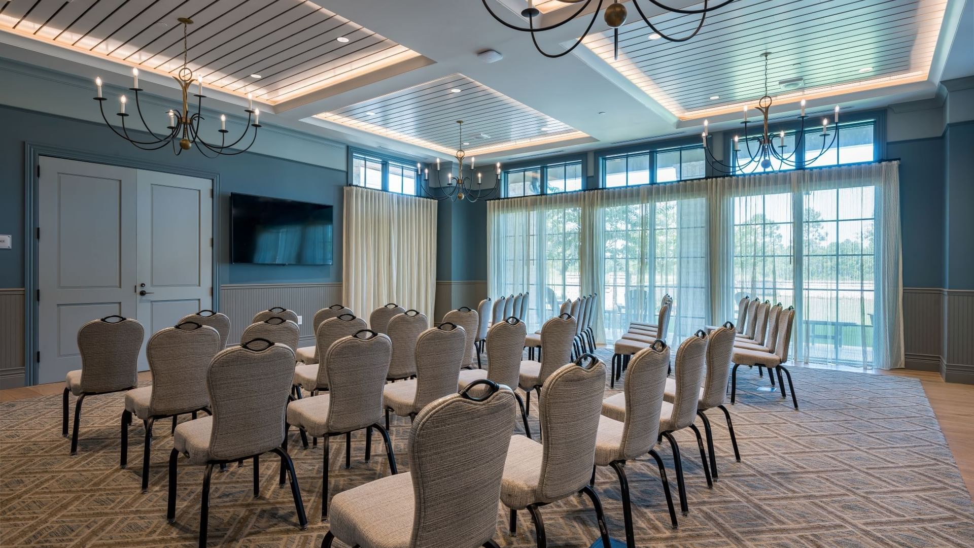 Club Room with rows of upholstered chairs, blue ceiling, chandeliers, and large windows at Camp Creek Inn in Inlet Beach