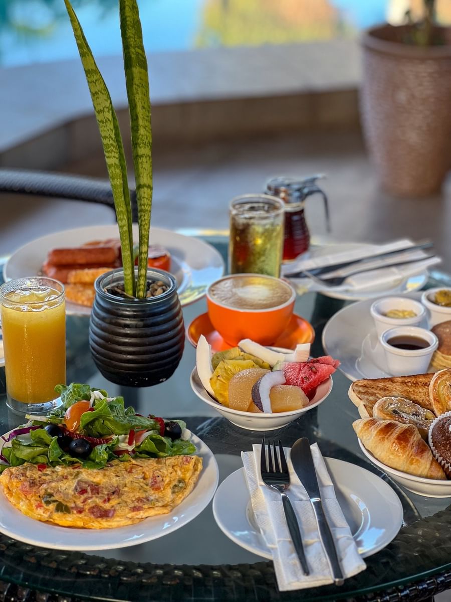 Fresh fruit, coffee, and pastries on a glass table by a small plant at TokaToka Resort Nadi Fiji