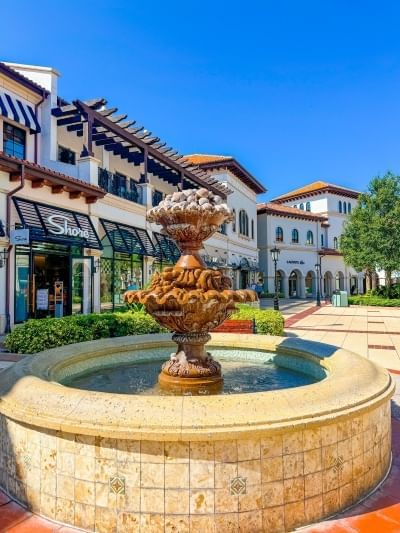 A beautiful stone fountain in a street surrounded by outdoor shops. 