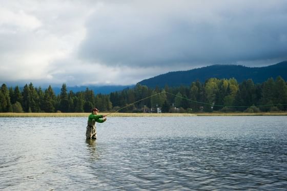 Fisherman standing in water with rod cast out and forest backdrop at Aava Whistler