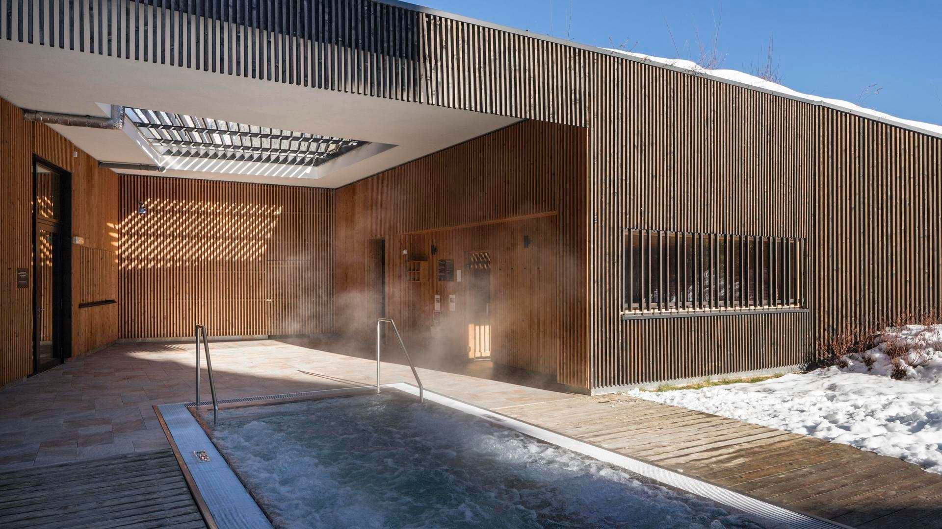 Steaming outdoor pool by a wooden building with snow around at Falkensteiner Hotel Schladming