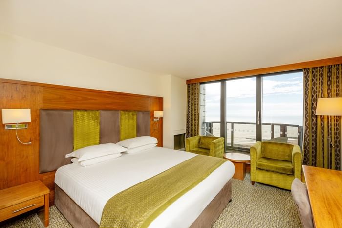 Modern double bedroom with sea view balcony, green accent furnishings and wood panelling at The View Hotel Eastbourne
