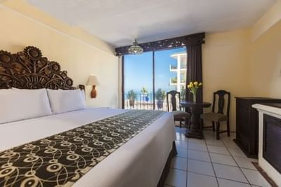 Hotel room with king bed, ornate headboard, balcony view of palm trees and ocean at Playa Los Arcos Puerto Vallarta