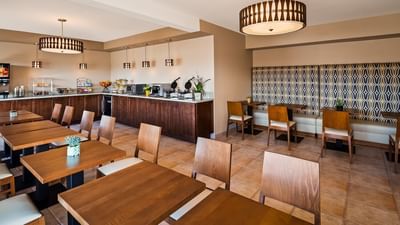 The spacious and well-lit indoor breakfast room with multiple wooden tables and a food counter at Carmel Bay View Inn