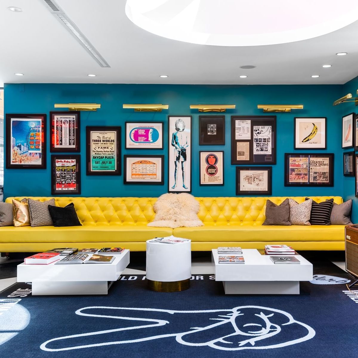 Vibrant hotel lounge with yellow tufted sofa, turquoise walls displaying framed music posters, and white coffee tables