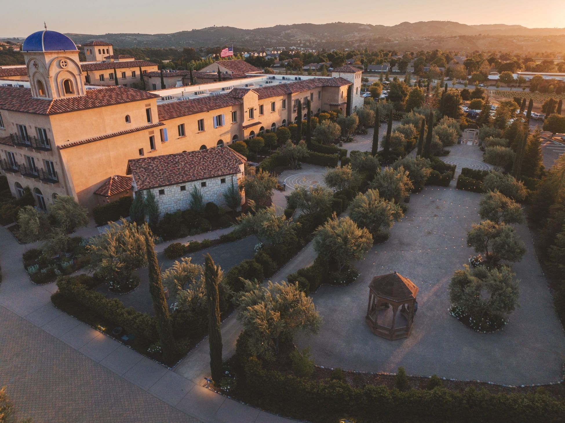 Lorem ipsum Wide view of hotel property. The hotel is on the left and it is surrounded by trees, garden and gazebo.