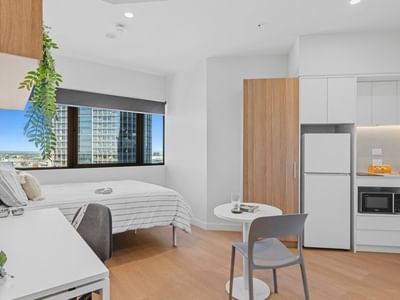 Modern studio apartment with bed, compact kitchenette, dining area, and city view at UniLodge Brisbane City