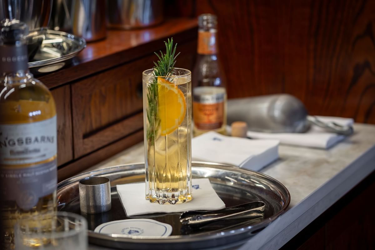 Highball cocktail with an orange slice and rosemary on a silver tray at the bar in Seaton House