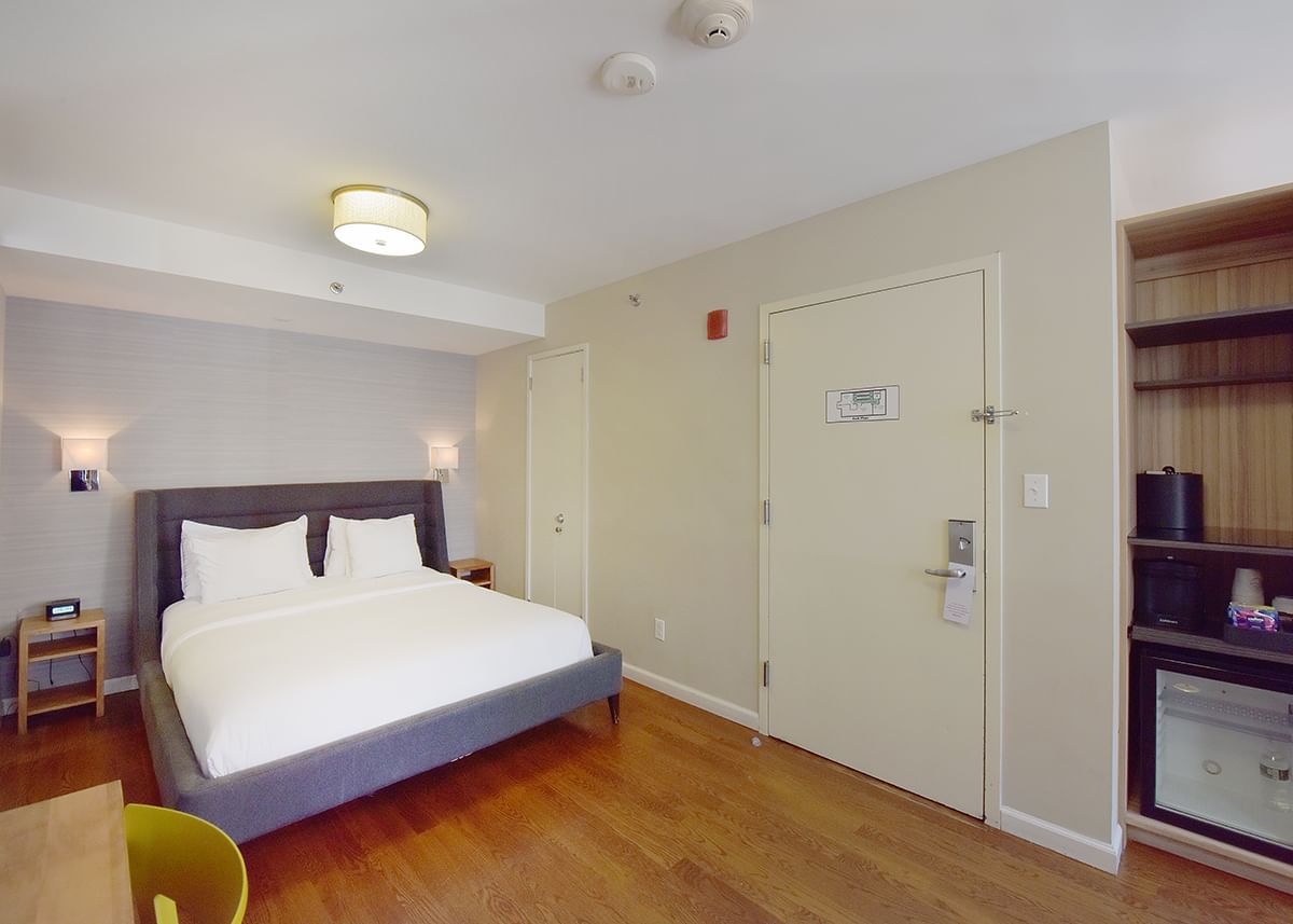 A hotel room with a bed, nightstand, and mini fridge.