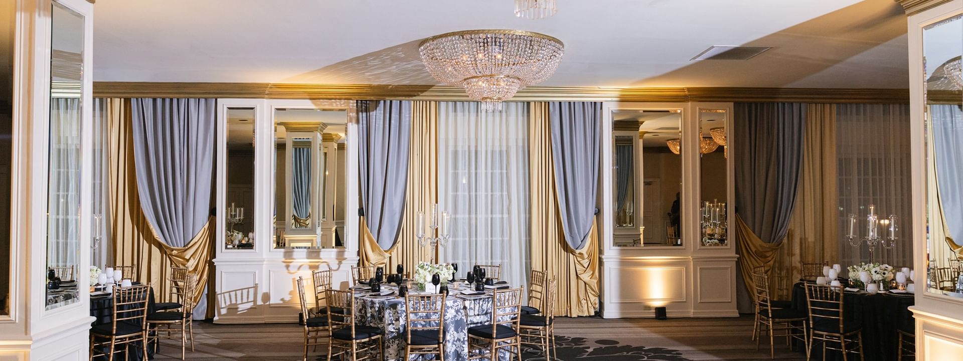 Event table by gold drapes under large crystal chandeliers in Crystal Ballroom at Warwick Melrose Dallas