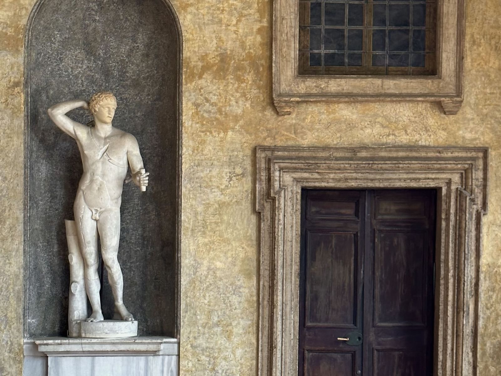 A marble statue in a niche beside an aged wooden door at Villa Medici near Margutta 19