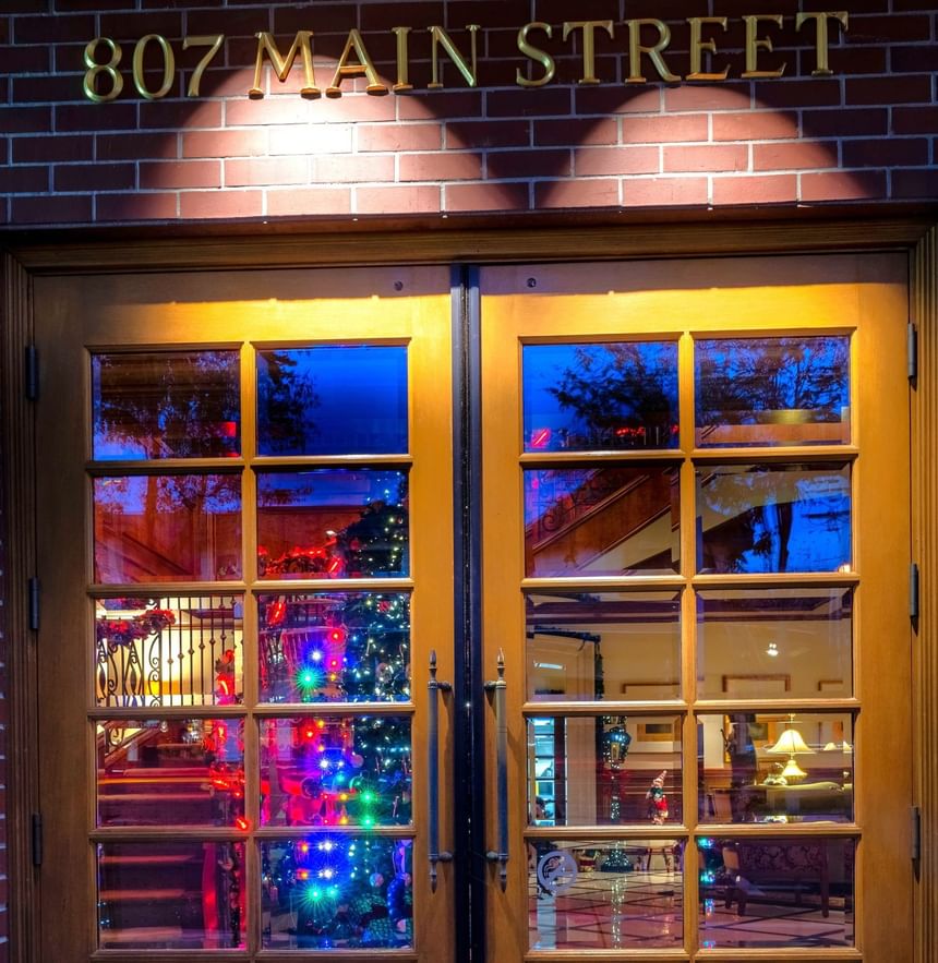 Entrance to The Rose Hotel features wooden double doors, reflecting colorful holiday lights and a Christmas tree inside