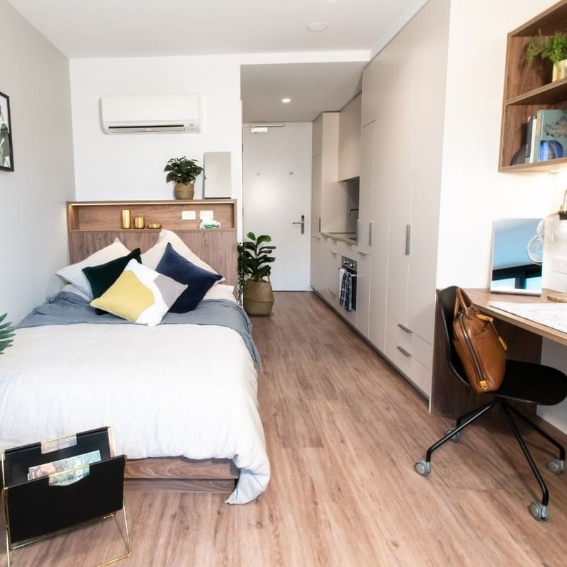 Compact studio with bed, desk, chair, shelves, and wooden floors, showcasing a minimalist and functional design.