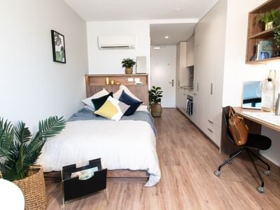 Compact studio with bed, desk, chair, shelves, and wooden floors, showcasing a minimalist and functional design.