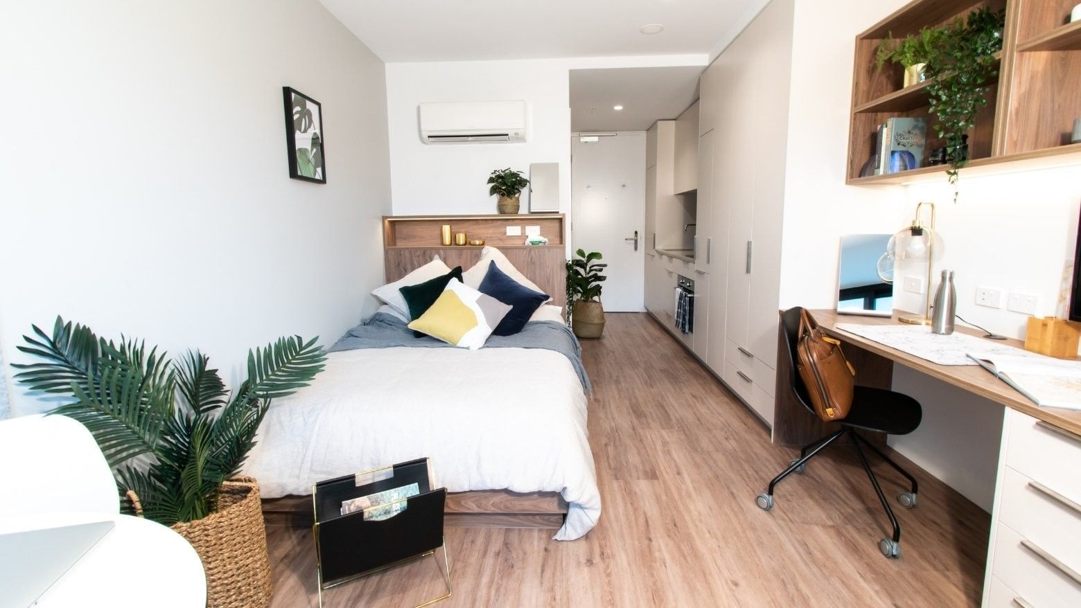 Compact studio with bed, desk, chair, shelves, and wooden floors, showcasing a minimalist and functional design.