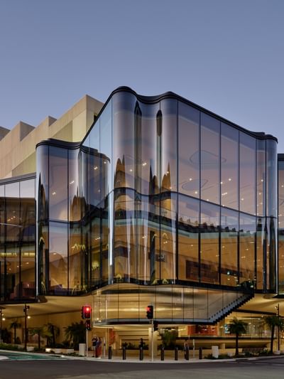 Modern curved glass facade of QPAC illuminated at dusk with reflective architectural panels and street-level entrance.