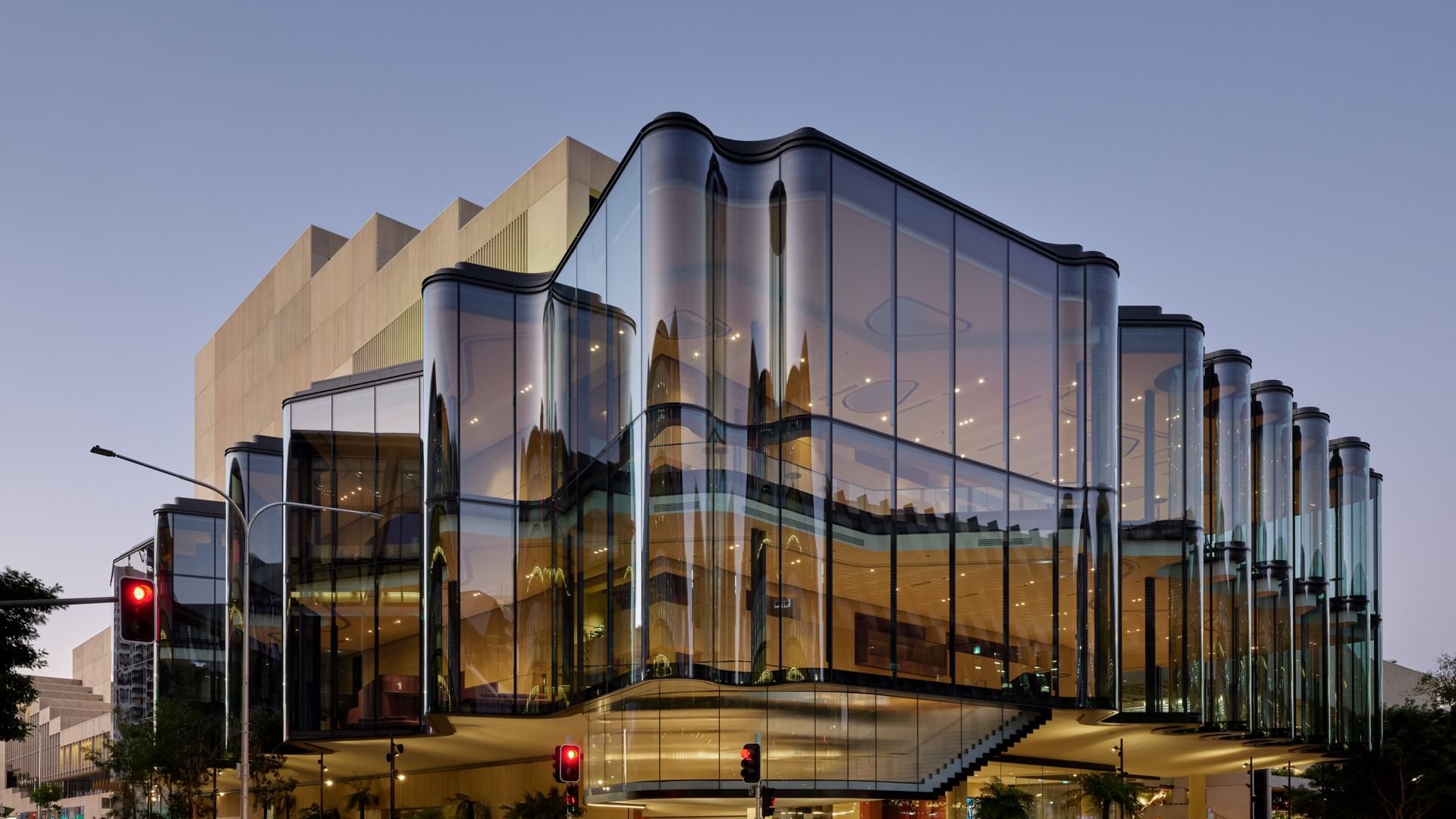 Modern curved glass facade of QPAC illuminated at dusk with reflective architectural panels and street-level entrance.
