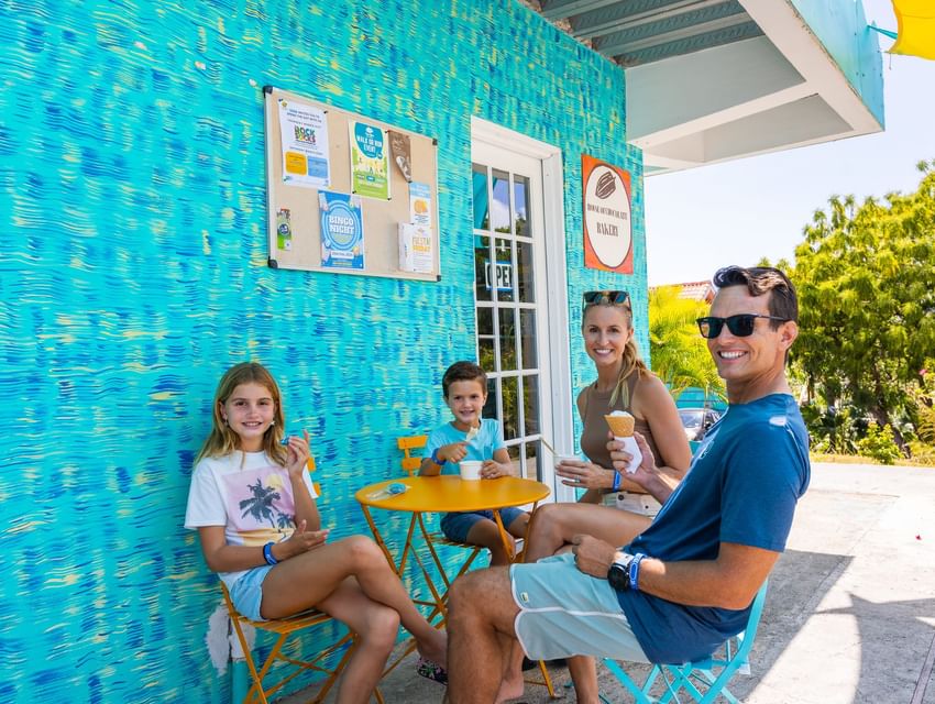 Family enjoying ice cream at yellow table on blue patio at True Blue Bay Hotel at House of Chocolate Bakery