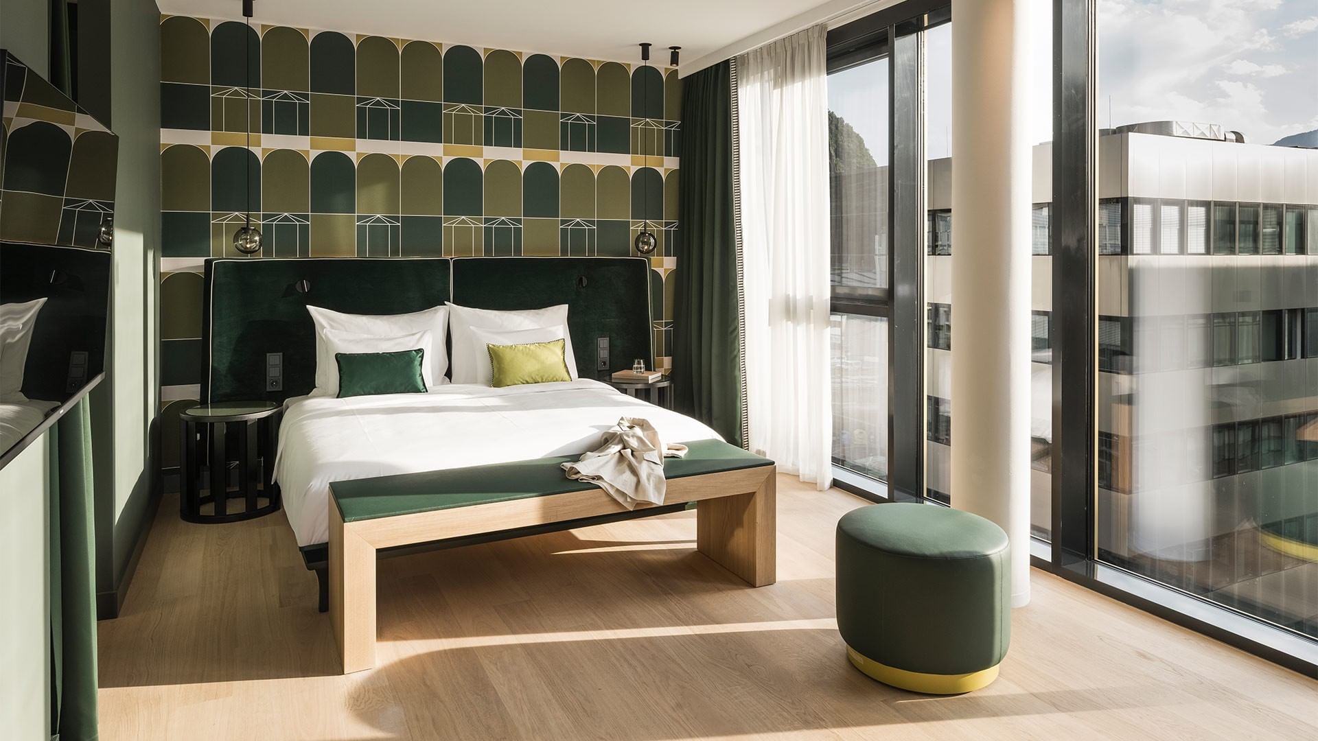 Junior Suite mit großem Bett, Bank und Fenstern am Falkensteiner Hotel Bozen WaltherPark in Bolzano.