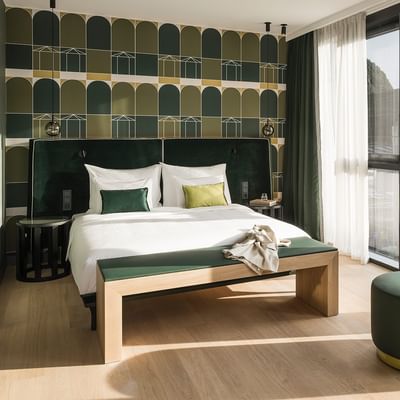 Junior Suite elegante con letto, divano e vista su edificio moderno a Bolzano presso Falkensteiner Hotel Bozen WaltherPark.