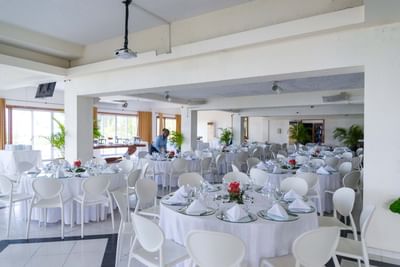 Staff arranging tables with white linens and red centerpieces near palm plants in Horizon Room at Hotel Montana Haiti