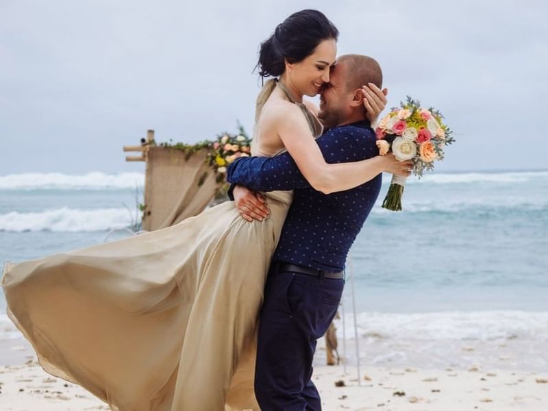 Novia y novio compartiendo un abrazo alegre sobre la arena tras una boda de lujo en Fiesta Americana Funeeq