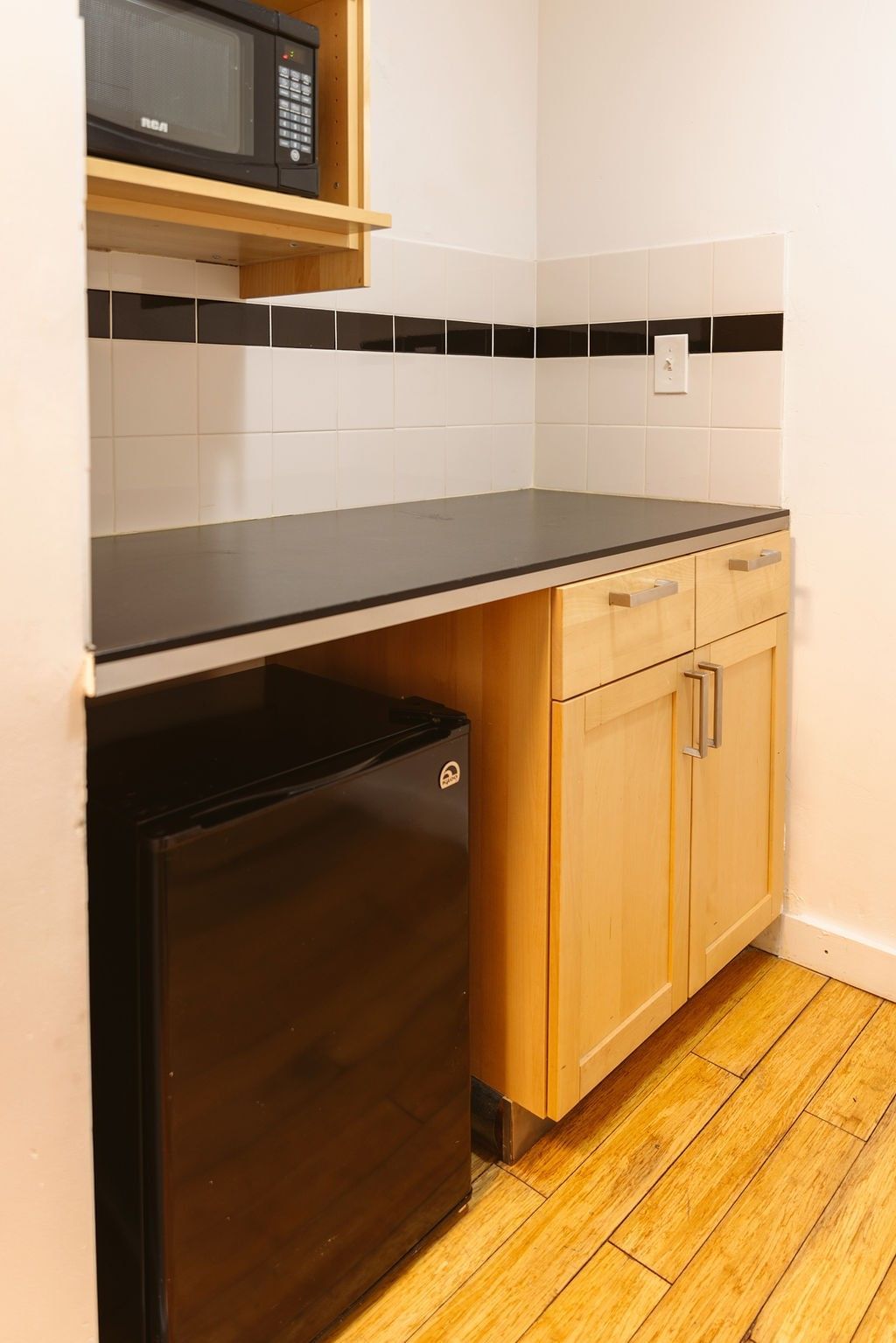 A small kitchenette with a microwave, mini fridge, and cabinets.