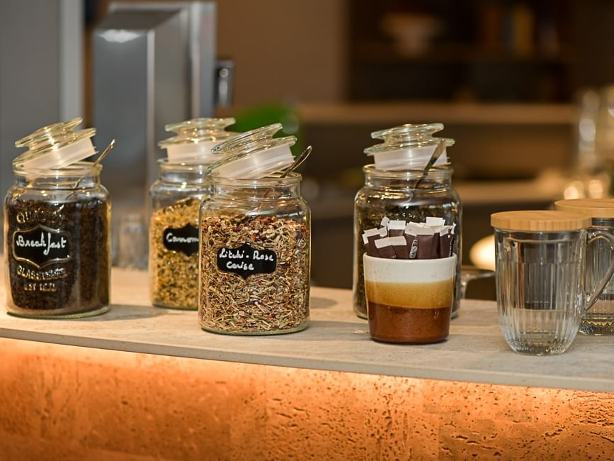 Bocaux de café et de thé variés sur un comptoir éclairé au Hôtel Rivella.