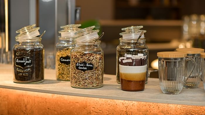 Bocaux de café et de thé variés sur un comptoir éclairé au Hôtel Rivella.
