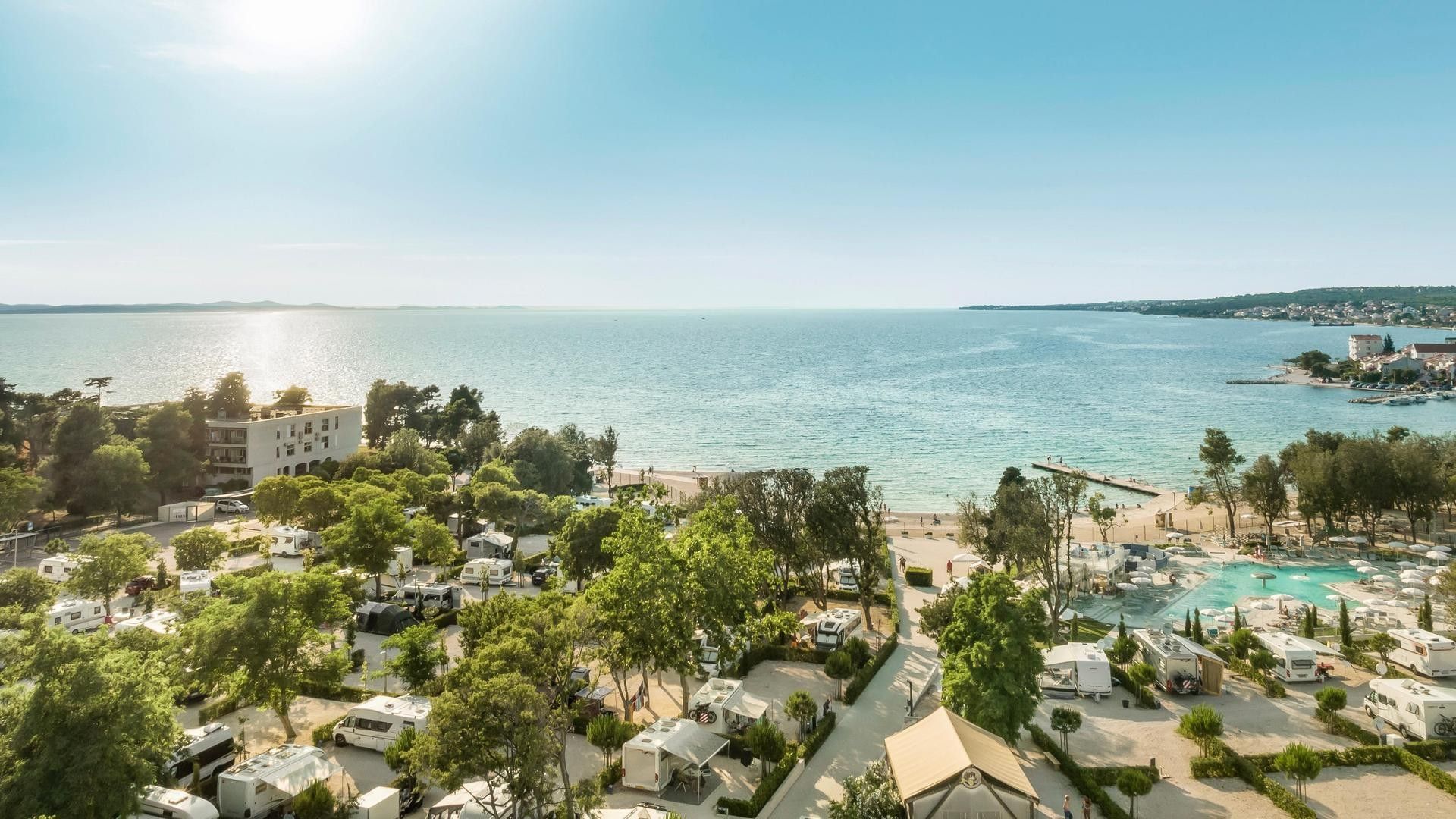 Pogled s visine na obalni kompleks s bazenom, kampom, plažom i tirkiznim morem u Falkensteiner Group