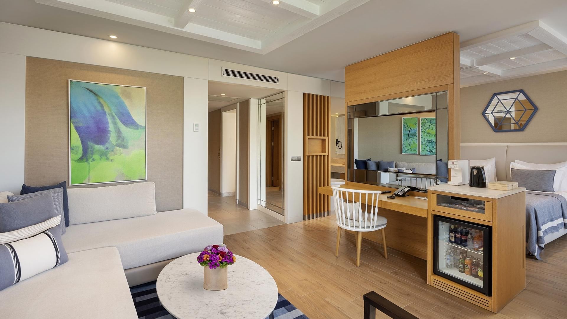 Luxurious Deluxe Sea View Room with couch, table, flowers, chair, desk, mini fridge, and a bed with pillows.