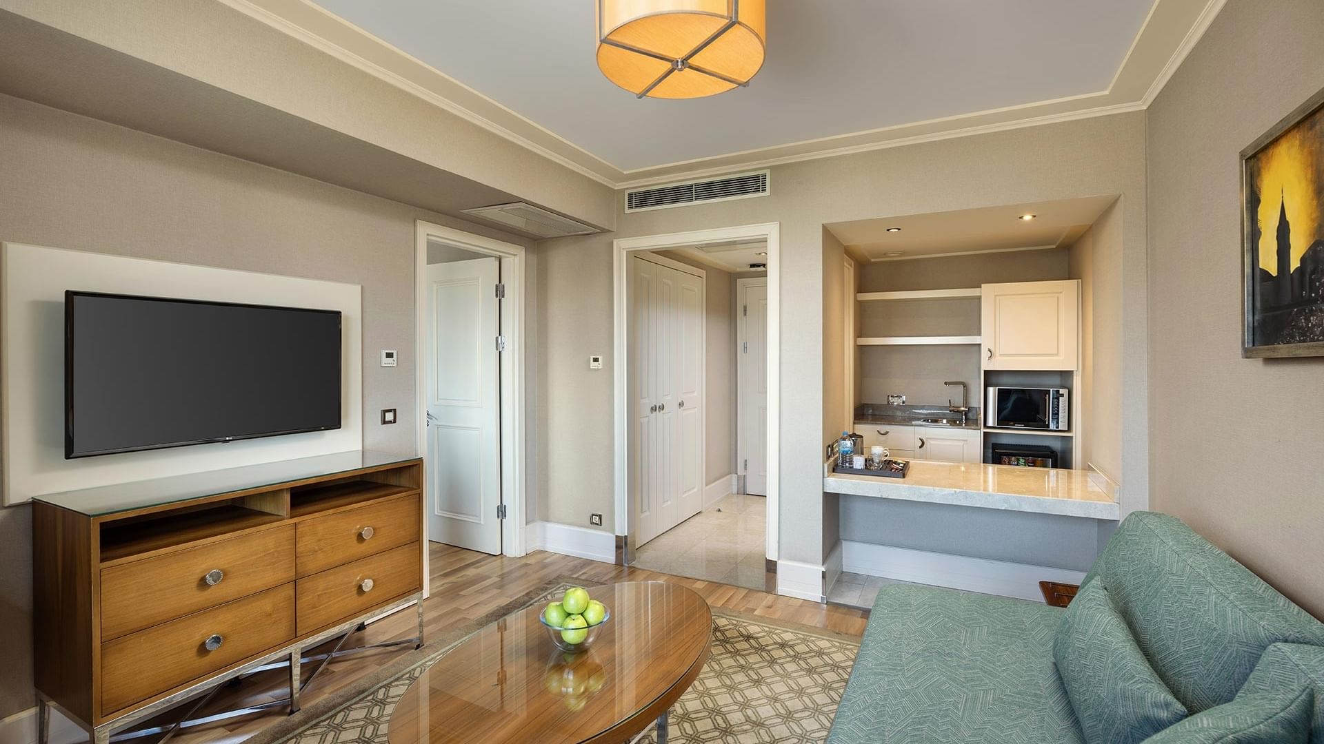 Living room with couch, coffee table, TV, and small kitchenette area in a Titanic City Taksim hotel suite.