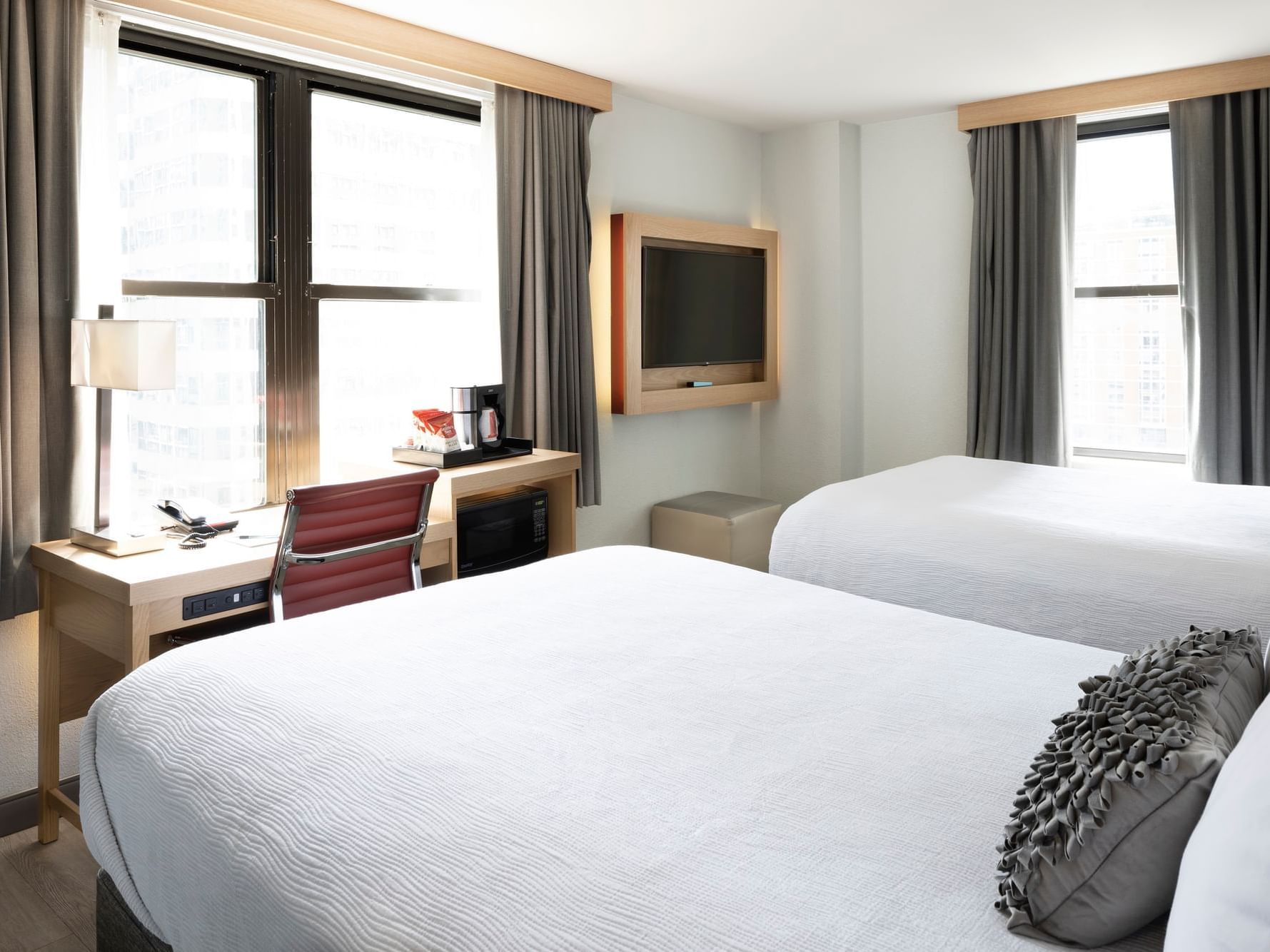 Hotel room with 2 beds, desk and chair, tv on wall with multiple windows. 