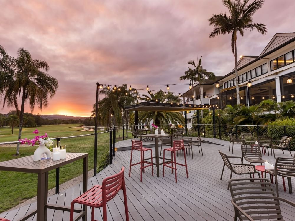 Outdoor patio with chairs and tables, string lights, and a view of a golf course at sunset.