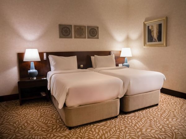 Two beds with nightstands and lamps in a hotel room at Saja by Warwick Makkah.