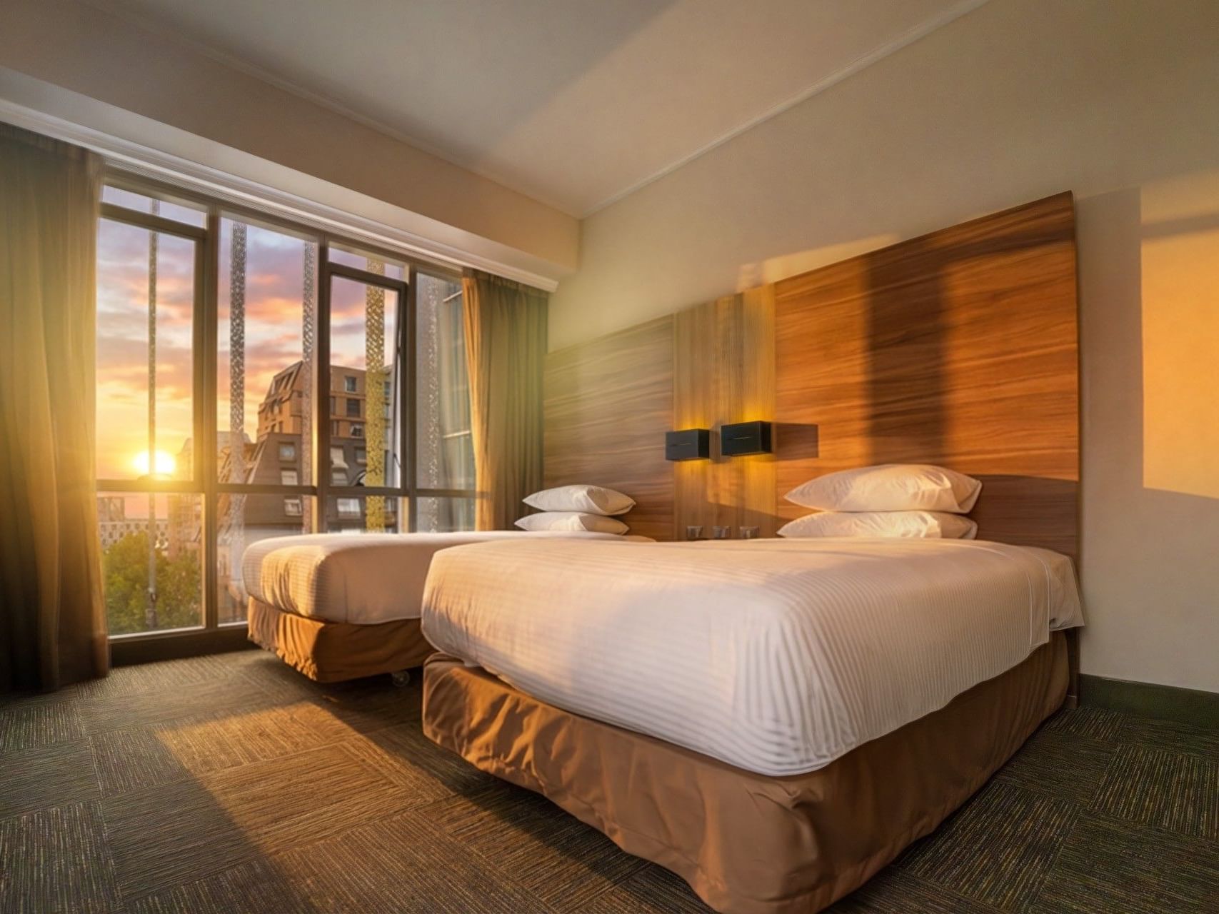Dos cómodas camas con vistas a la puesta de sol a través de los amplios ventanales del hotel HCC Costanera Concepción.