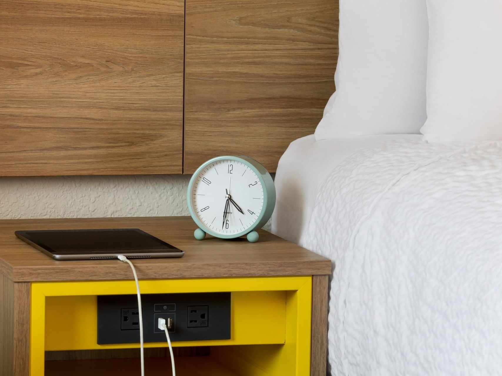 Close up of a clock & a tab on tabletop by the bed at Hotel Bo