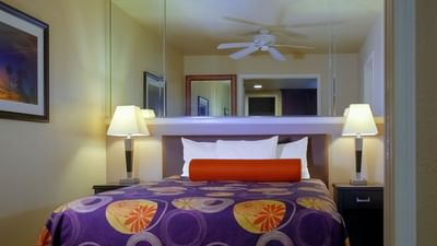 Guest room with purple patterned bedding, white pillows, orange accent pillow, and bedside lamps at London Bridge Resort