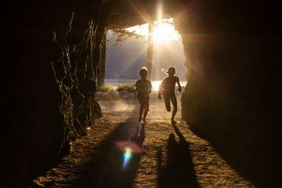 Two children run out of a cave towards the setting sun.