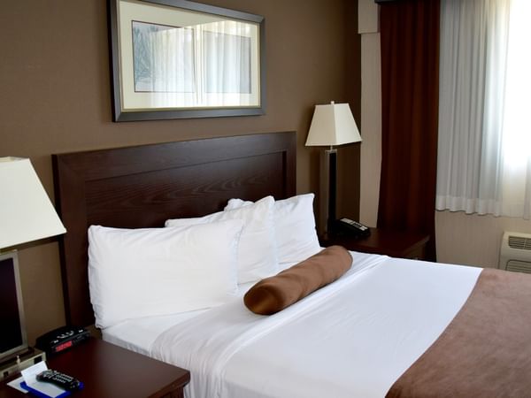 A cozy hotel room with a bed, two nightstands with lamps, and a window with curtains.