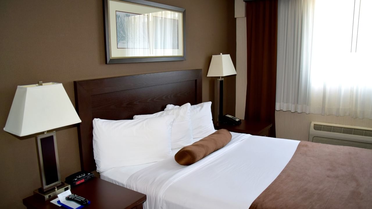 A cozy hotel room with a bed, two nightstands with lamps, and a window with curtains.